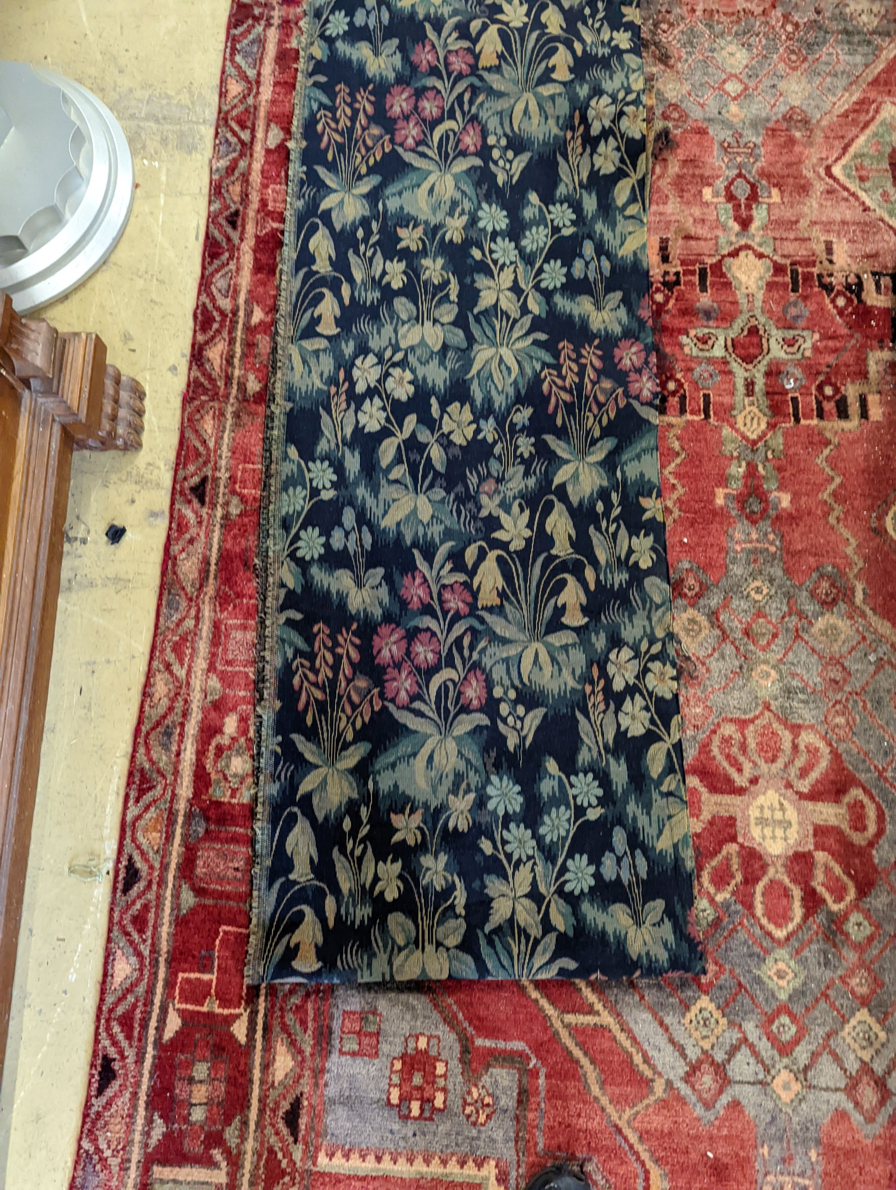 Length of machine tapestry fabric with flowers on a black ground, 420 x 52cm together with a Caucasian rug faced cushion and an antique English needlework panel with stylised scrolls 175 x 67cm
